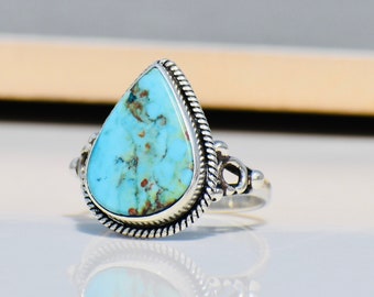 May include: A teardrop-shaped turquoise ring set in sterling silver. The turquoise is a light blue color with brown and black veins.