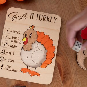 May include: Wooden "Roll a Turkey" game with a turkey illustration and dice. The game board has the text "Roll a Turkey" and numbered sections for the turkey's body parts. A hand is rolling a die.