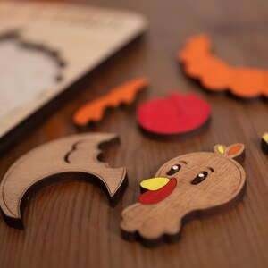 May include: Wooden puzzle pieces in various shapes and colors, including a turkey, a crescent moon, a tomato, and a pumpkin. The pieces are scattered on a wooden surface, with the puzzle base visible in the background. A fun, educational toy.