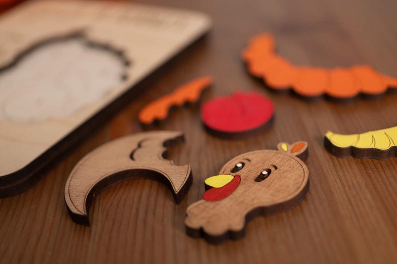 May include: Wooden puzzle pieces in various shapes and colors, including a turkey, a crescent moon, a tomato, and a pumpkin. The pieces are scattered on a wooden surface, with the puzzle base visible in the background. A fun, educational toy.