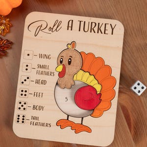 May include: Wooden "Roll a Turkey" game board with a cartoon turkey illustration. The board includes dice symbols and body part labels. A die and a wooden leaf are next to the board. The text "Roll a Turkey" is at the top.