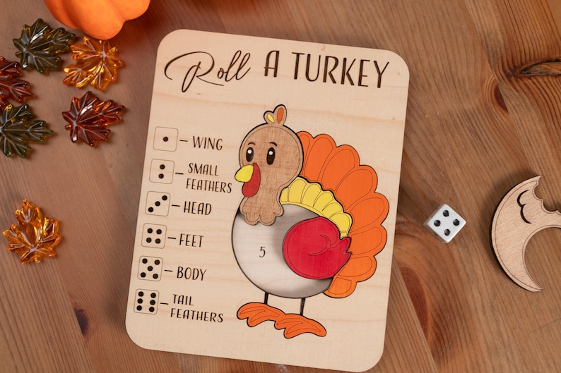 May include: Wooden "Roll a Turkey" game board with a cartoon turkey illustration. The board includes dice symbols and body part labels. A die and a wooden leaf are next to the board. The text "Roll a Turkey" is at the top.