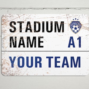 May include: White metal sign with a distressed look. The sign says "Stadium Name A1 Your Team" with a blue soccer ball logo.