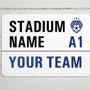 May include: White sign with blue and gold text and a blue and gold soccer ball logo. The sign reads "STADIUM NAME A1 YOUR TEAM".