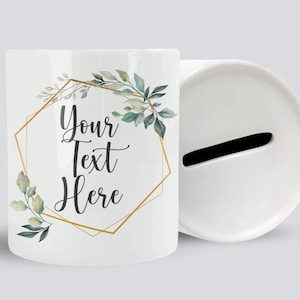 May include: White ceramic money box with a gold geometric frame and green watercolour leaves. The text "Your Text Here" is written in black inside the frame.