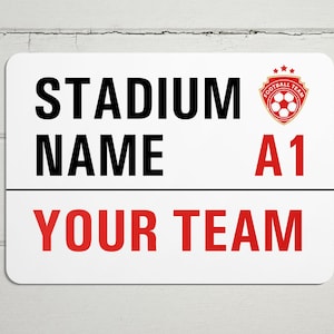 May include: White sign with black text that reads "STADIUM NAME A1 YOUR TEAM". A red and gold soccer logo is in the top right corner.