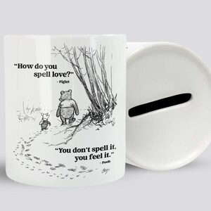 May include: White ceramic money box featuring a black and white illustration of Winnie the Pooh and Piglet walking in the woods. The quote "How do you spell love? - Piglet" is printed above the illustration. The quote "You don't spell it, you feel it. - Pooh" is printed below the illustration.