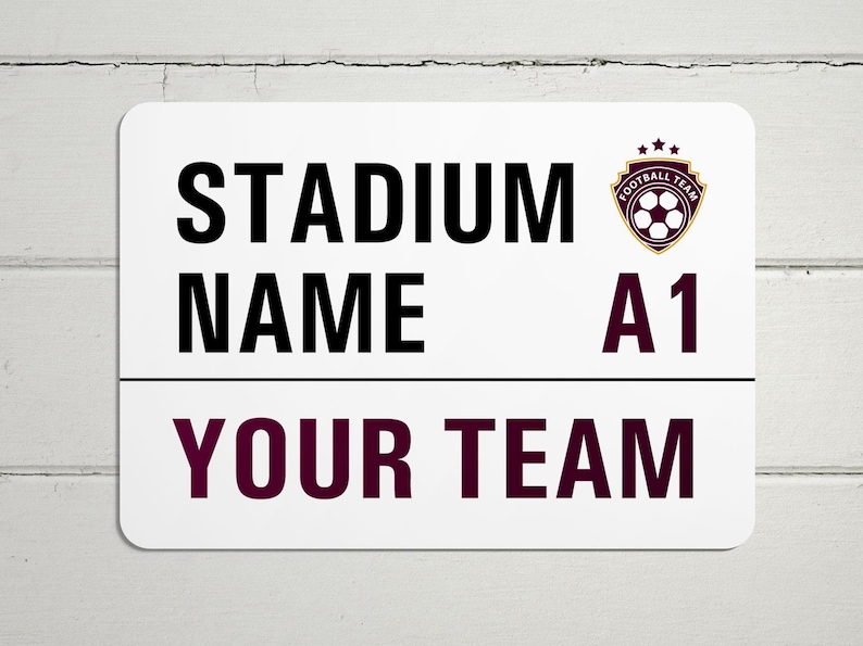 May include: White sign with black text that reads "Stadium Name A1 Your Team". A burgundy and gold soccer ball logo is in the top right corner.