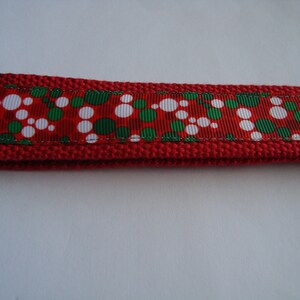 May include: Red key fob with a ribbon featuring white and green polka dots. The key fob has a red knitted border and a silver-coloured metal clasp.