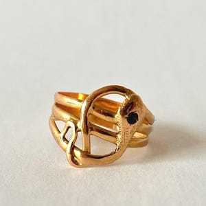 Op de afbeelding: Een goudkleurige ring met een gestileerd olifantenontwerp. De ring heeft een gedetailleerde olifantenkop met een kleine zwarte steen voor het oog. De ring heeft een ontwerp met drie banden voor extra visuele interesse.