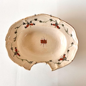 Peut inclure: Plat de service en céramique blanc cassé avec un bord festonné. Le plat présente un motif peint à la main de motifs floraux rouges et verts sur le bord et une libellule au centre. Le plat a un aspect légèrement vieilli.