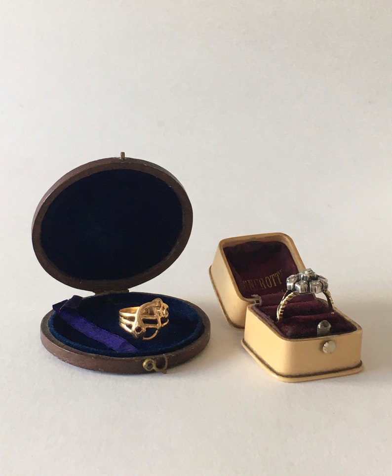 Op de afbeelding: Twee ringendozen, een bruine met een gouden ring erin en een beige met een diamanten ring erin. De beige doos heeft de tekst "Tiffany & Co." erop.