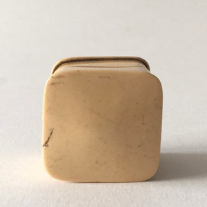 Op de afbeelding: Een klein, vierkant, ivoren doosje met een licht afgeronde bovenkant. Het doosje is gemaakt van glad, cr&egrave;mekleurig ivoor en heeft een subtiele glans.