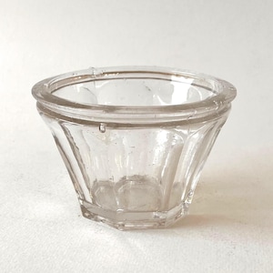 May include: A clear glass bowl with a wide, circular rim and a faceted, multi-sided base. The vessel features vertical panels along its exterior walls, creating a structured, geometric appearance with a smooth, transparent finish throughout.