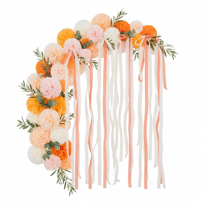 May include: A semi-circular floral arrangement featuring orange, peach, pink, and white pom-poms, accented with green foliage. Long, flowing ribbons in white and peach cascade downwards, creating a decorative and festive display.