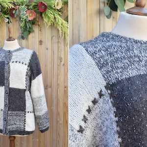 Könnte beinhalten: Ein grauer, weißer und schwarzer Patchwork-Cardigan mit Knopfleiste. Der Cardigan hat eine strukturierte Strickware und ist aus Wolle.
