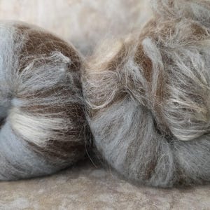 May include: Two skeins of yarn in shades of brown, gray, and white. The yarn is fluffy and soft, and it is perfect for knitting or crocheting.