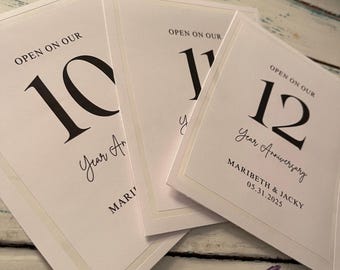 May include: Three white cards with black text. The cards read "Open on our" followed by the numbers 10, 11, and 12, and "Year Anniversary." The bottom card includes names and a date.