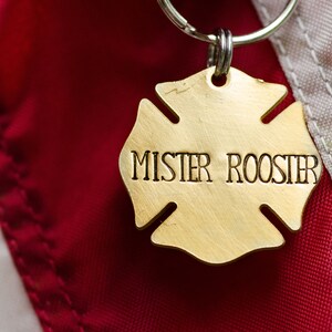 May include: A gold-colored metal keychain shaped like a four-pointed star with the words "Mister Rooster" engraved on it. The keychain is attached to a silver key ring.