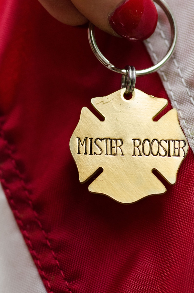 May include: A gold-colored metal keychain shaped like a four-pointed star with the words "Mister Rooster" engraved on it. The keychain is attached to a silver key ring.