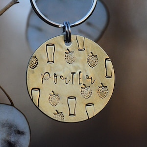 May include: A gold-colored metal keychain with a round tag featuring the word "PORTER" and a pattern of beer mugs and hops.