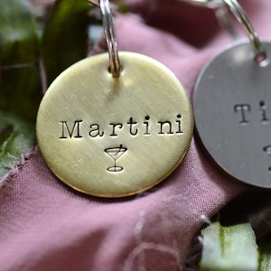 May include: Two circular metal tags with key rings. The gold-toned tag is stamped with the word Martini and a small cocktail glass icon. The silver-toned tag is stamped with the word Tini and a matching small cocktail glass icon below the text.