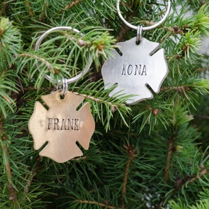 May include: Two silver firefighter helmet-shaped keychains with rings. One keychain is gold and says "FRANK" and the other is silver and says "KONA".