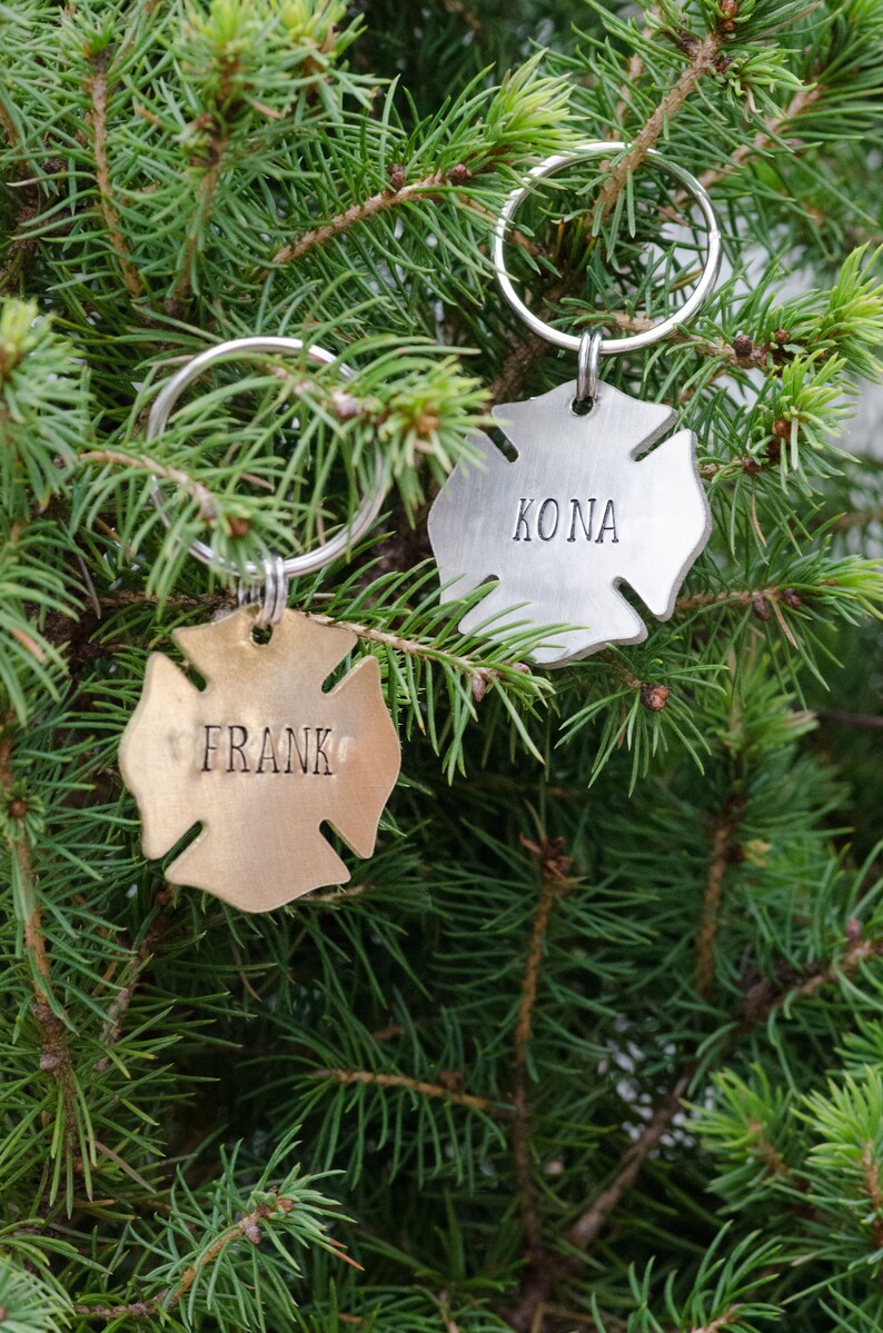 May include: Two silver firefighter helmet-shaped keychains with rings. One keychain is gold and says "FRANK" and the other is silver and says "KONA".