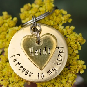 May include: A gold-toned metal keychain with a heart-shaped charm engraved with the name "Heidi" and the words "forever in my heart".
