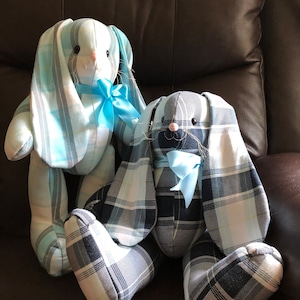 May include: Two plush bunny toys, one with blue and white plaid fabric and a blue bow, the other with black and white plaid fabric and a blue bow.