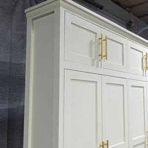 May include: White cabinet with six doors and gold-toned handles. The cabinet has a raised trim around the top and a simple, clean design.