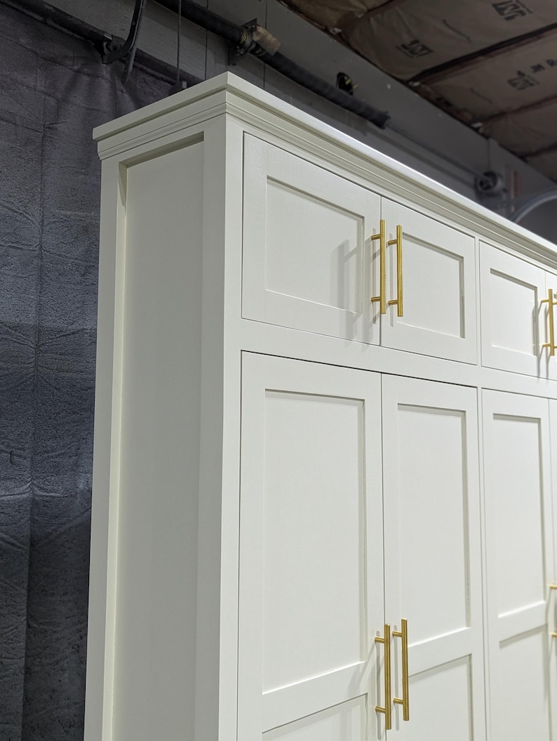 May include: White cabinet with six doors and gold-toned handles. The cabinet has a raised trim around the top and a simple, clean design.