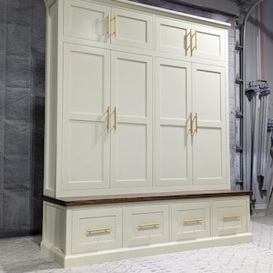 May include: A white cabinet with six doors and four drawers. The cabinet has gold-coloured handles. The cabinet is sitting on a wooden floor.