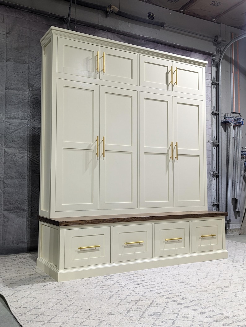 May include: A white cabinet with six doors and four drawers. The cabinet has gold-coloured handles. The cabinet is sitting on a wooden floor.
