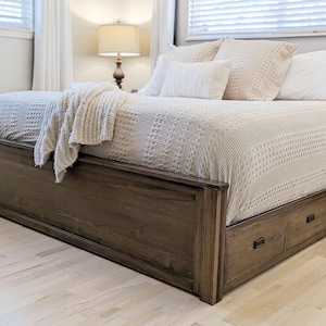 May include: A wooden bed frame with a white bedspread and pillows. The bed frame has storage drawers underneath.