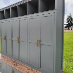 May include: A gray wooden storage cabinet with a bench and multiple doors. The cabinet has a wood top and gold door handles.