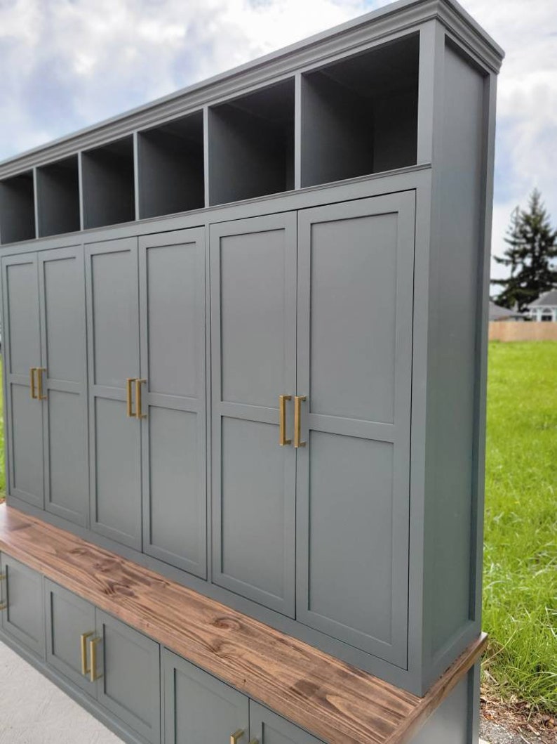 May include: A gray wooden storage cabinet with a bench and multiple doors. The cabinet has a wood top and gold door handles.