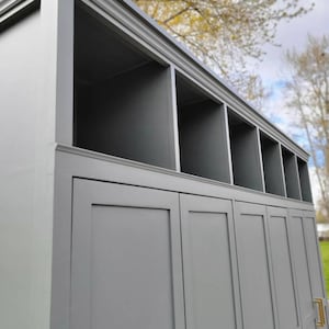 May include: A gray wooden cabinet with three doors and a top shelf with open cubbies. The cabinet has gold door handles.