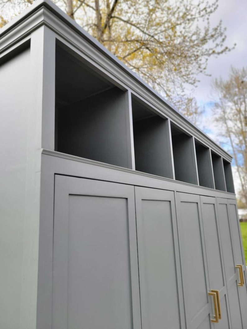 May include: A gray wooden cabinet with three doors and a top shelf with open cubbies. The cabinet has gold door handles.