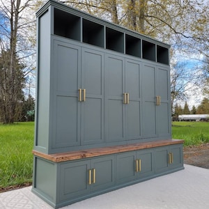 May include: A tall, dark green wooden storage cabinet with a bench seat and multiple doors and shelves. The cabinet has gold-toned hardware.