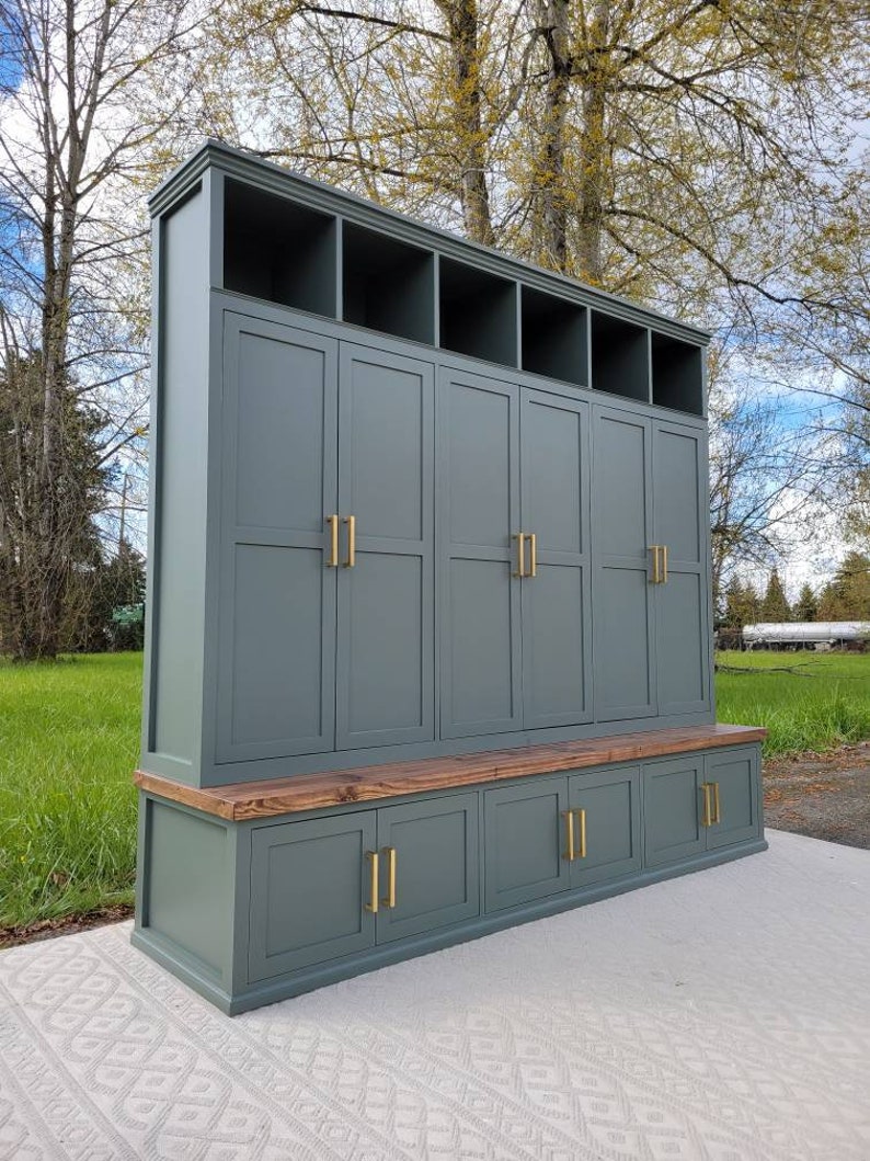 May include: A tall, dark green wooden storage cabinet with a bench seat and multiple doors and shelves. The cabinet has gold-toned hardware.