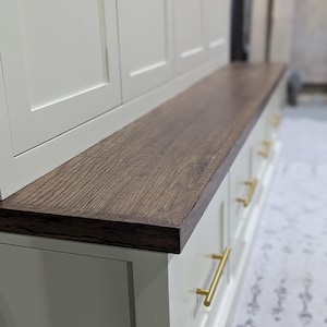May include: White cabinet with a wood top and gold drawer pulls. The cabinet has three doors and a bench top.