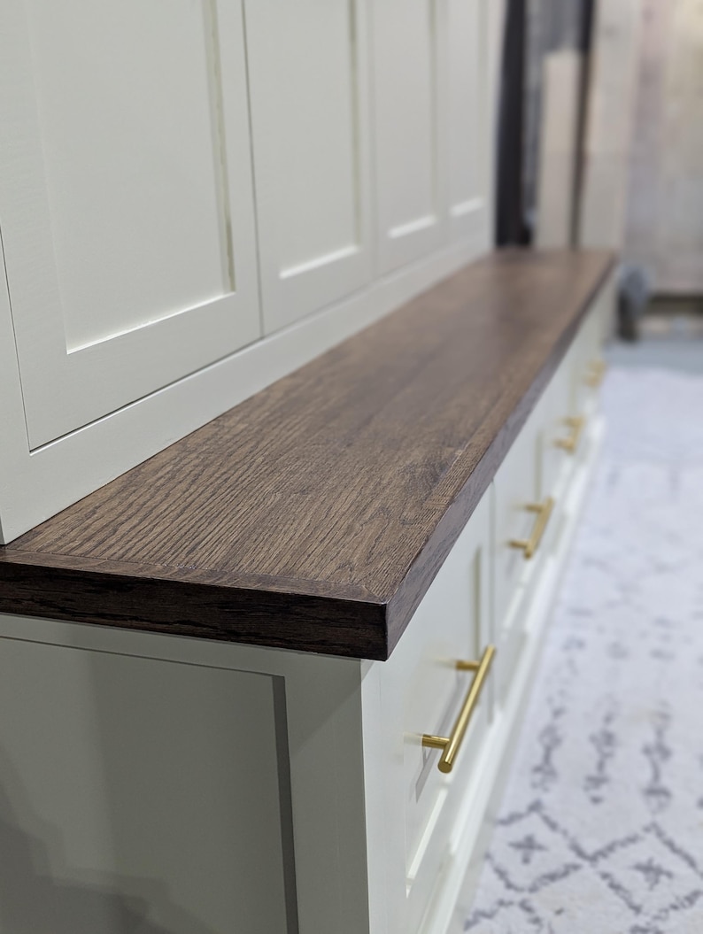 May include: White cabinet with a wood top and gold drawer pulls. The cabinet has three doors and a bench top.