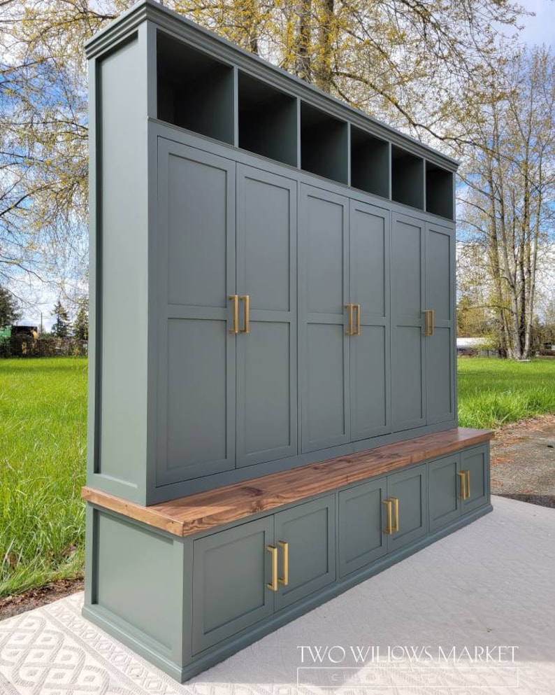 May include: A green painted wooden storage bench with a wood top and multiple doors and shelves. The bench has gold door handles and the text "TWO WILLOWS MARKET" is visible on the bottom right corner.