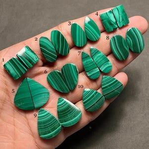 May include: Ten pairs of polished malachite gemstones in diverse shapes, including rectangles, ovals, and teardrops. The gemstones exhibit a vibrant green hue with distinctive banded patterns. The malachite stones are displayed on a hand.