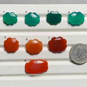 May include: Eight cloud-shaped gemstones in shades of green and orange, displayed on a white surface. A quarter coin is included for size reference. The gemstones have a glossy finish and varying color intensities.