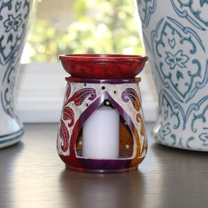 May include: A colorful, carved stone oil burner with a white candle inside. The burner has a red, orange, purple, and white design.