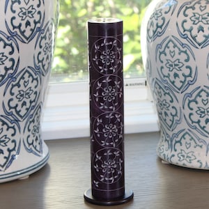 May include: Purple carved stone incense burner with a floral design. The burner is on a black wooden base.