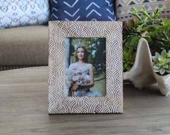 May include: A wooden picture frame with a white and brown geometric pattern. The frame is holding a photo of a person with a bouquet of flowers.