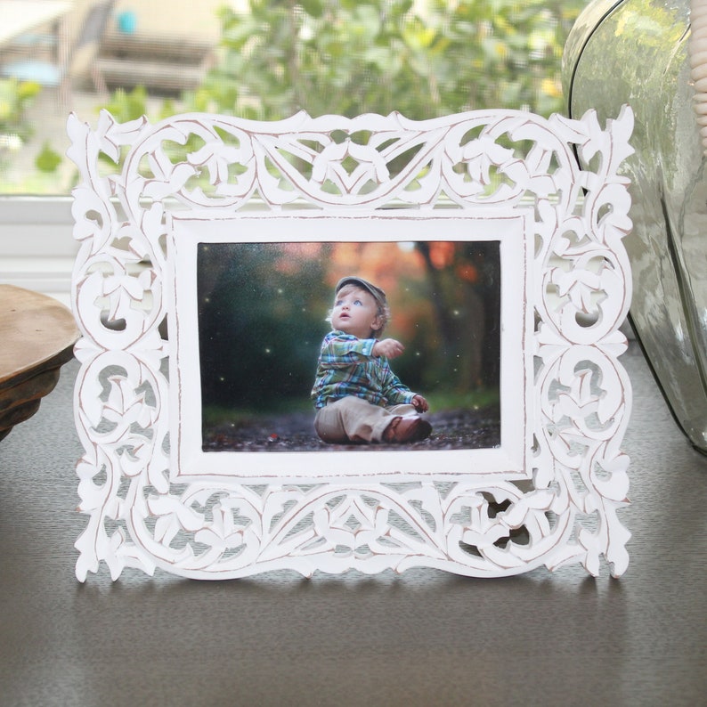 May include: White wooden picture frame with an intricate carved design. The frame is holding a photo of a young child looking up at the sky.